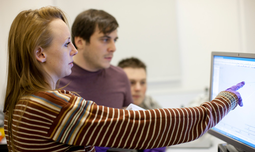 Female research supervisor pointing at a computer screen while two male researchers look on