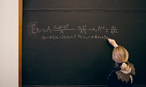 Blonde haired lecturer writing equation on blackboard