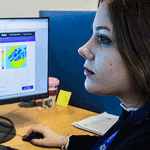 A researcher analysing scientific data on dual computer monitors in an office setting.