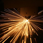 Bright sparks flying from a manufacturing or welding process in a dark environment.