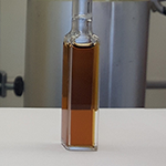 Glass vial containing coloured liquid, set against a laboratory background with tubing and equipment.
