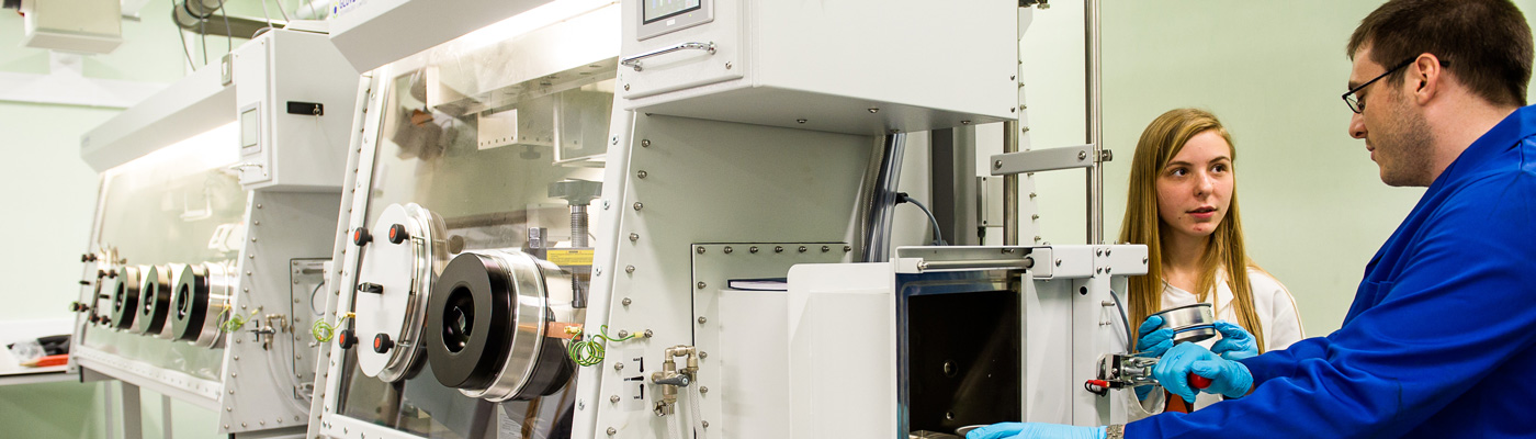 Researchers in lab coats talking to each other stood next to white equipment