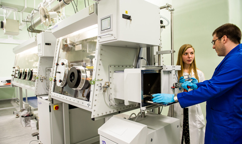 Researchers in lab coats talking to each other stood next to white equipment